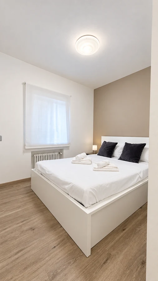 Camera matrimoniale di Alkecè Red con letto bianco, cuscini neri e finestra