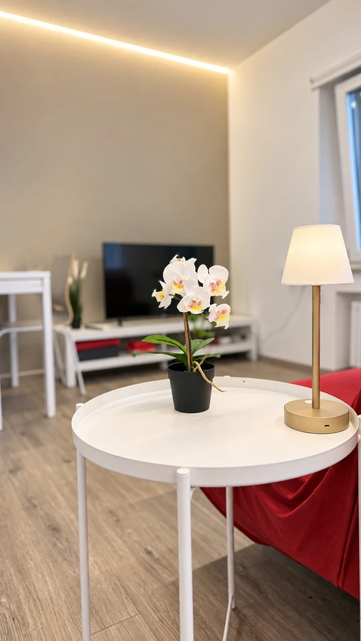 Tavolino bianco con orchidea e lampada accanto al divano rosso di Alkecè Red