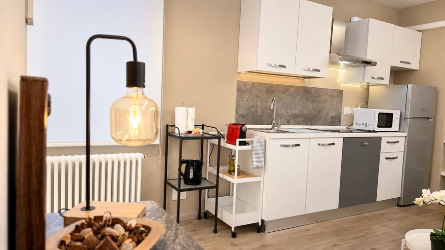 Cucina attrezzata di Alkecè White con frigorifero e microonde, con una lampada a filamento in primo piano